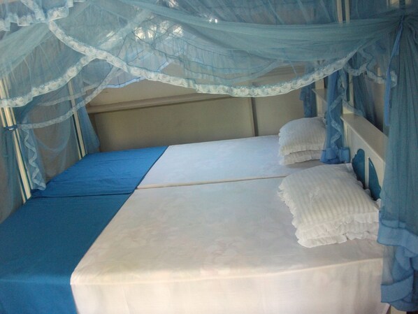 Una cama individual con colchón blanco y colcha azul, un dosel con detalles de encaje y un cabecero.