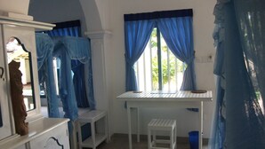 A room with a white desk, blue curtains, and a small white stool. - Zimmer Rest (Unawatuna)