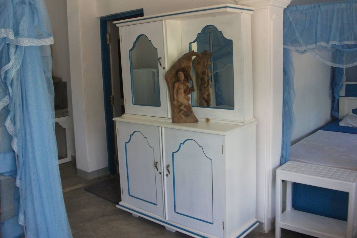 A bedroom with a white wardrobe, a bed with blue bedding, and a blue curtain.