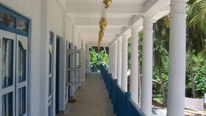 A corridor with white and blue doors, a hanging lamp, and columns. - Zimmer Rest (Unawatuna)