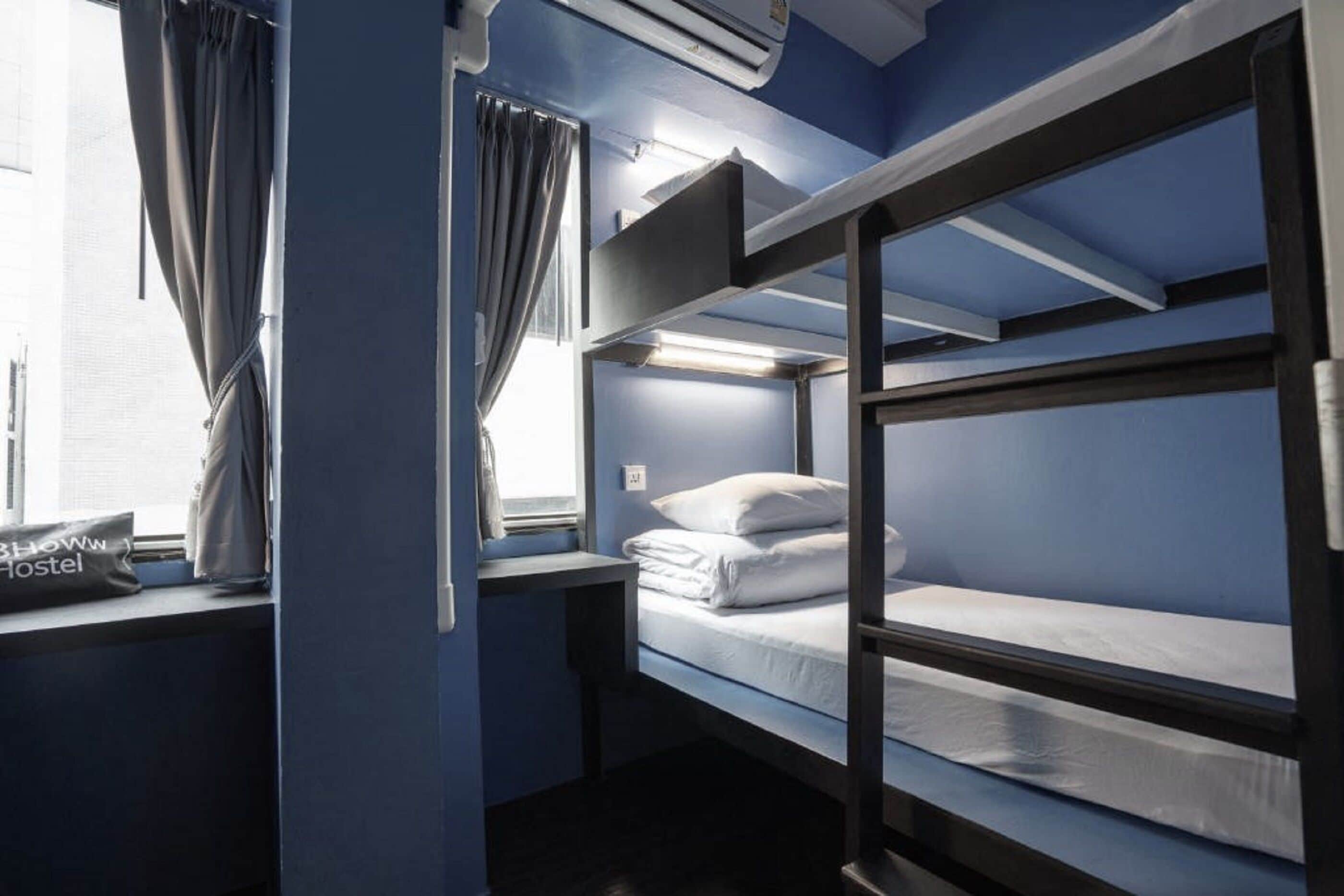 Een slaapkamer met een stapelbed, een raam, gordijnen en een tas met de tekst 'SHOWROOM HOSTEL'.