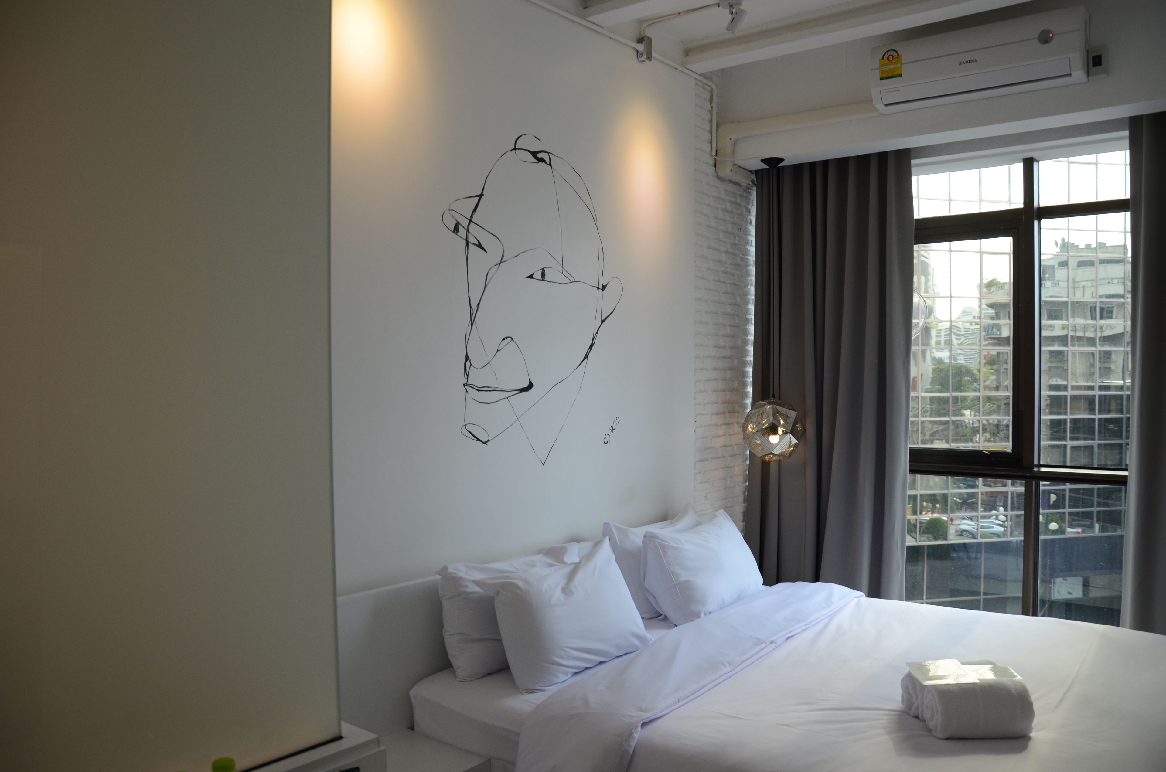 A modern hotel room with a large window, a white bed, and a unique abstract wall art piece.
