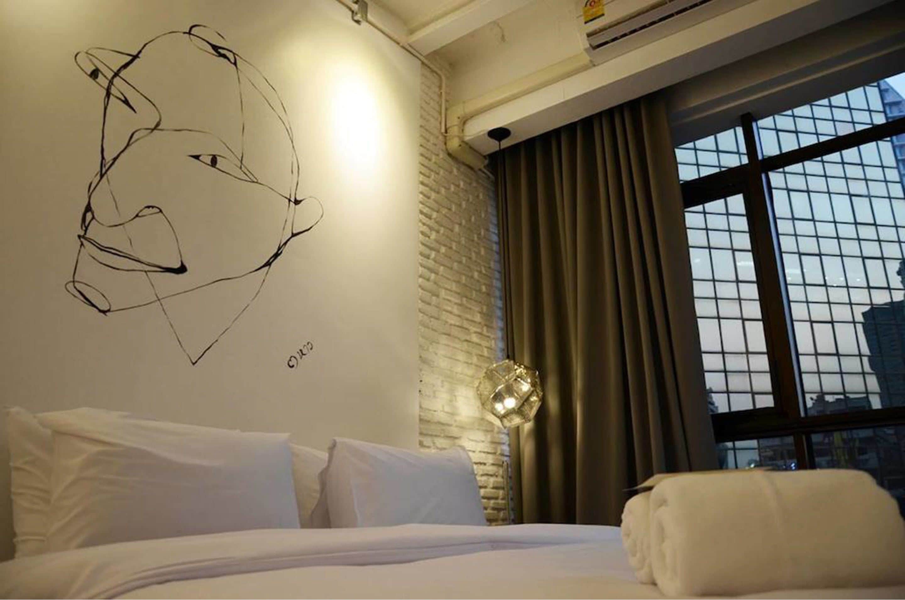 Quarto de hotel com cama, obra de arte abstrata na parede, janela com cortinas e vista para a cidade.