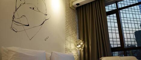 Quarto de hotel com cama, obra de arte abstrata na parede, janela com cortinas e vista para a cidade.