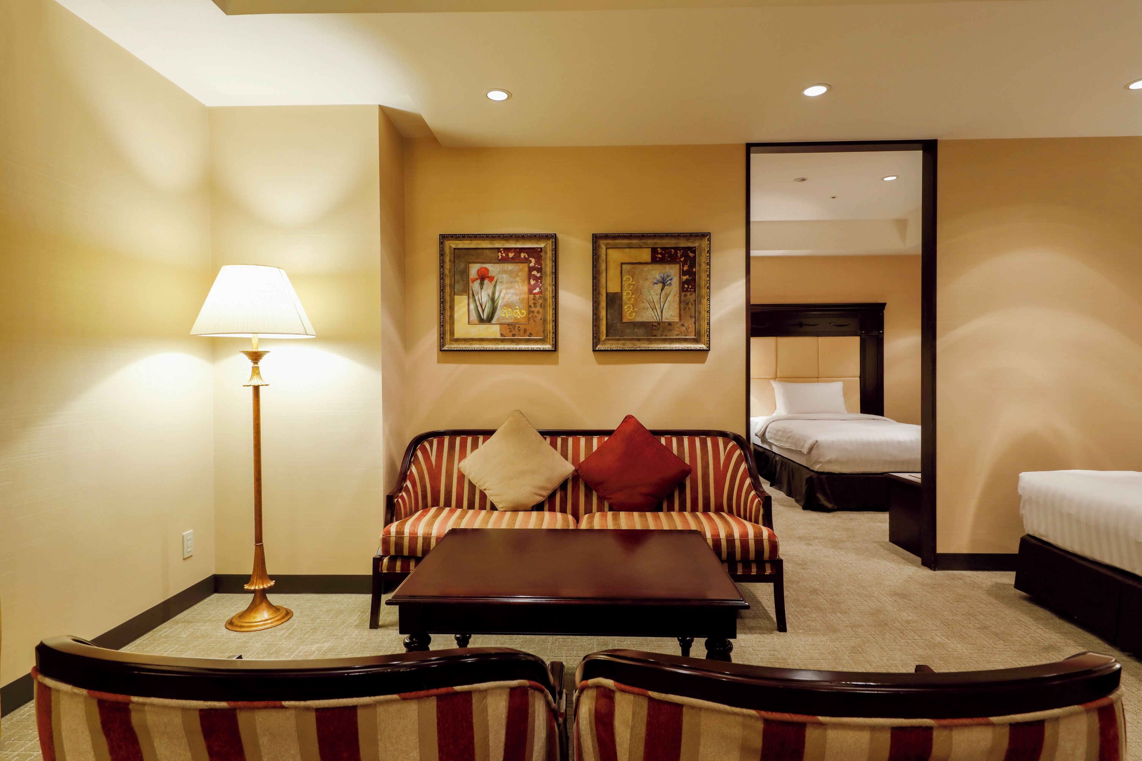 A hotel room with a sofa, two beds, a coffee table, and a lamp.