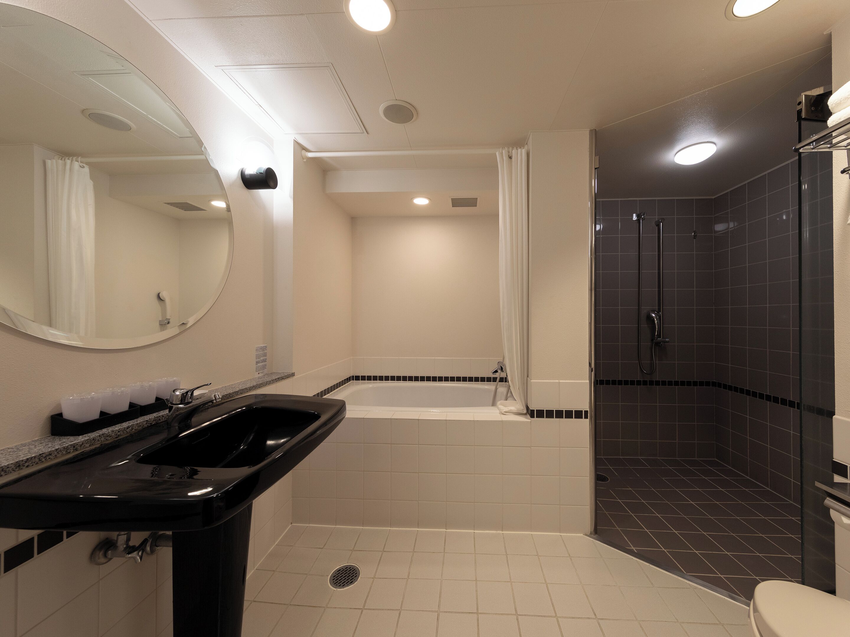 A modern bathroom with a black sink, a bathtub, and a shower area.