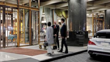 A hotel entrance with a glass door, a luggage cart, and a white car parked outside.