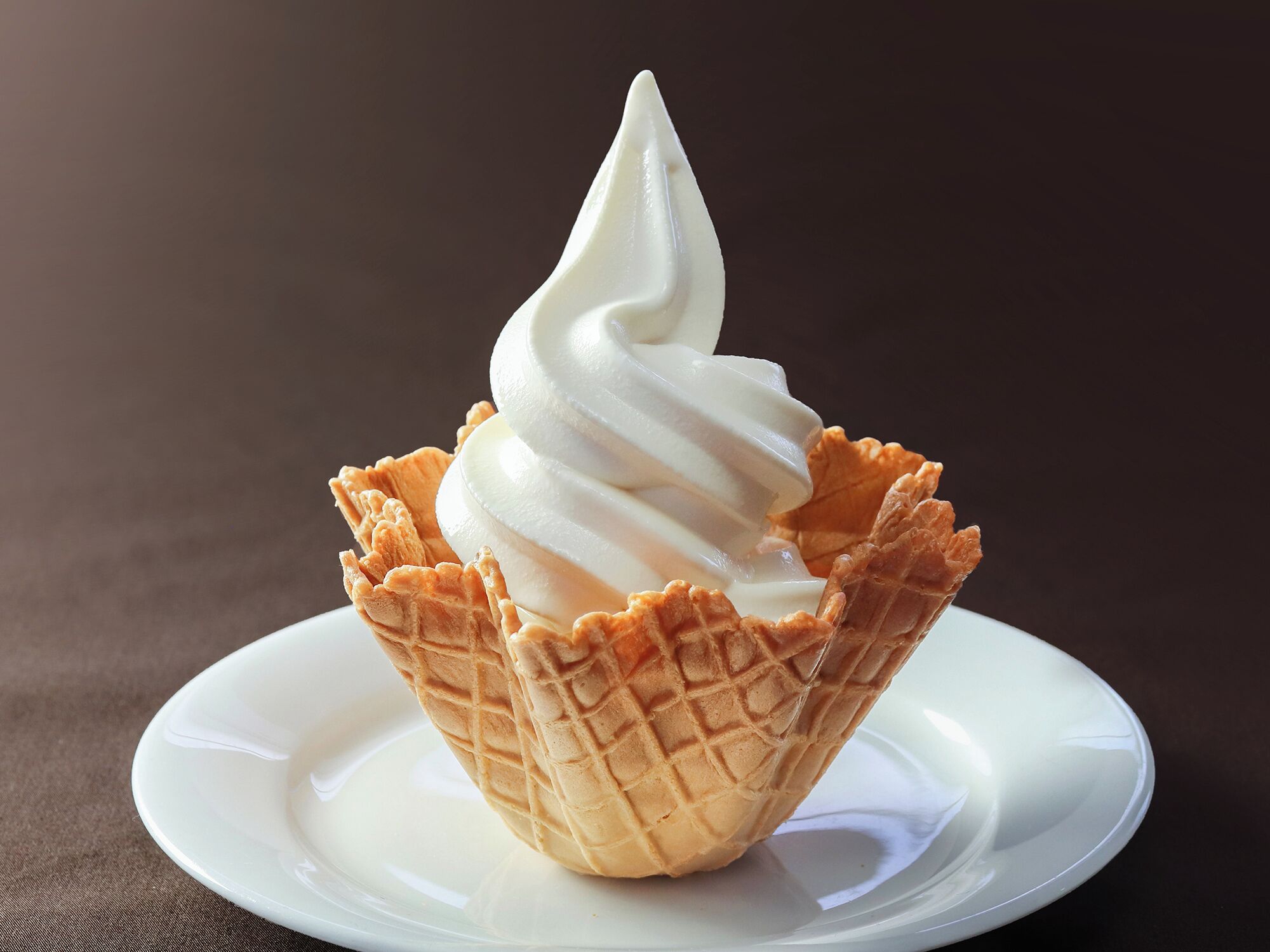 A waffle cone filled with white ice cream on a white plate.