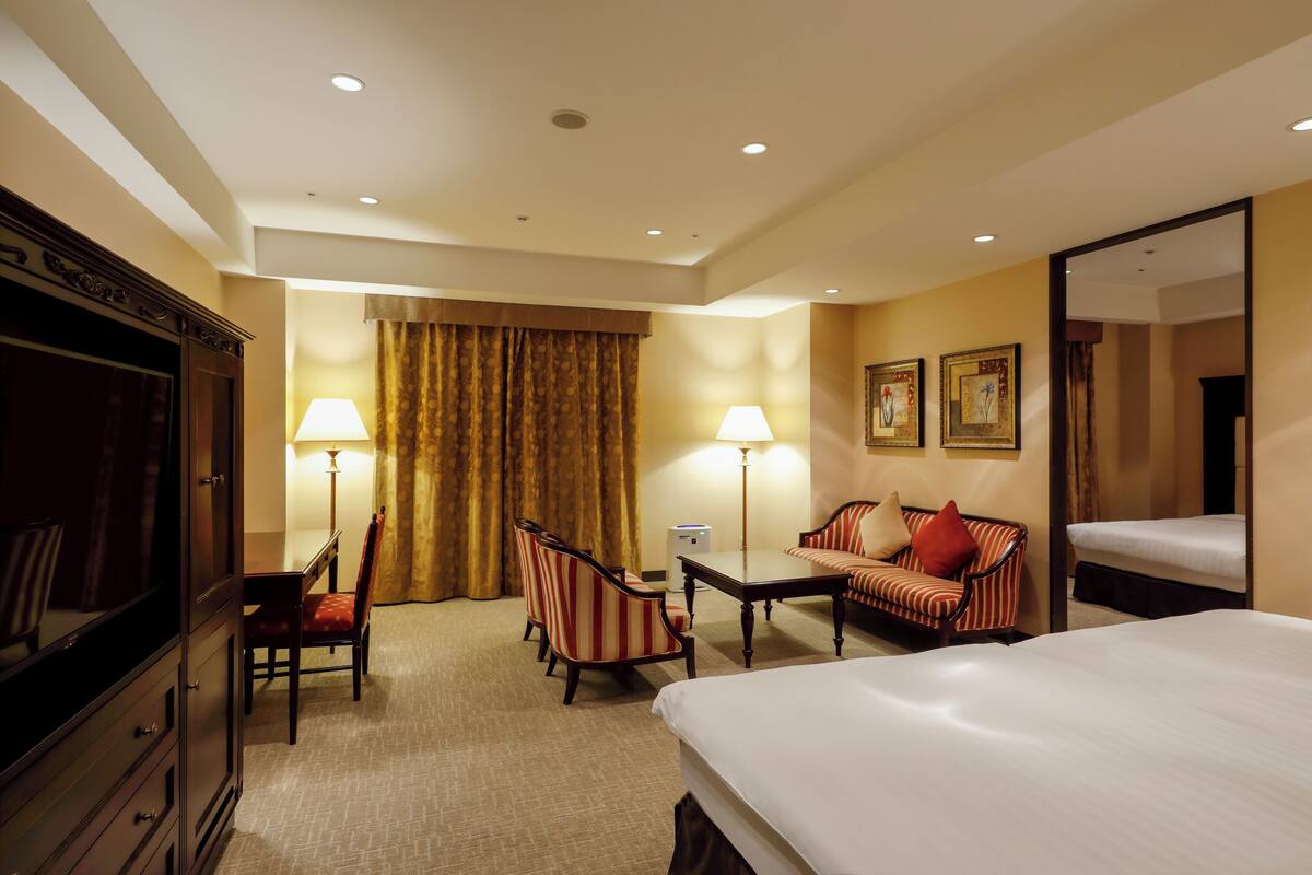 Habitación de hotel con cama, escritorio, dos sillas, sofá, lámpara, espejo y armario.