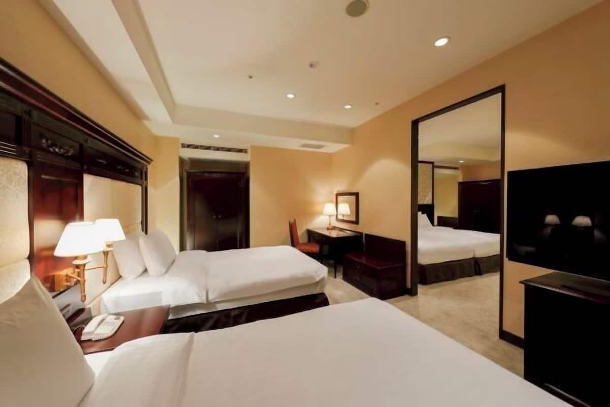Habitación de hotel con dos camas, un escritorio, una silla, un televisor y un espejo.