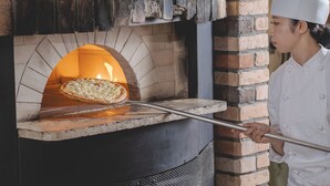 A brick oven pizza oven with a pizza inside, a chef in a white uniform, and a pizza peel in front of it. - Premier Hotel Tsubaki Sapporo (Sapporo)
