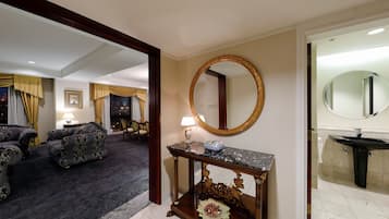 A hotel room with a living area, a dining table, and a bathroom with a sink and mirror.