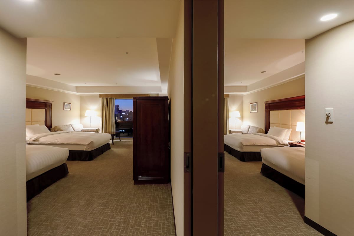 Habitación de hotel con dos camas, vista al paisaje urbano y puerta que da a otra habitación.