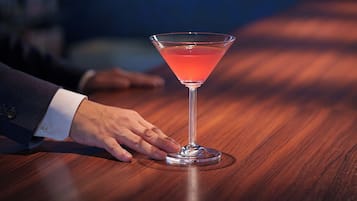 A martini glass on a wooden table with a hand reaching towards it.