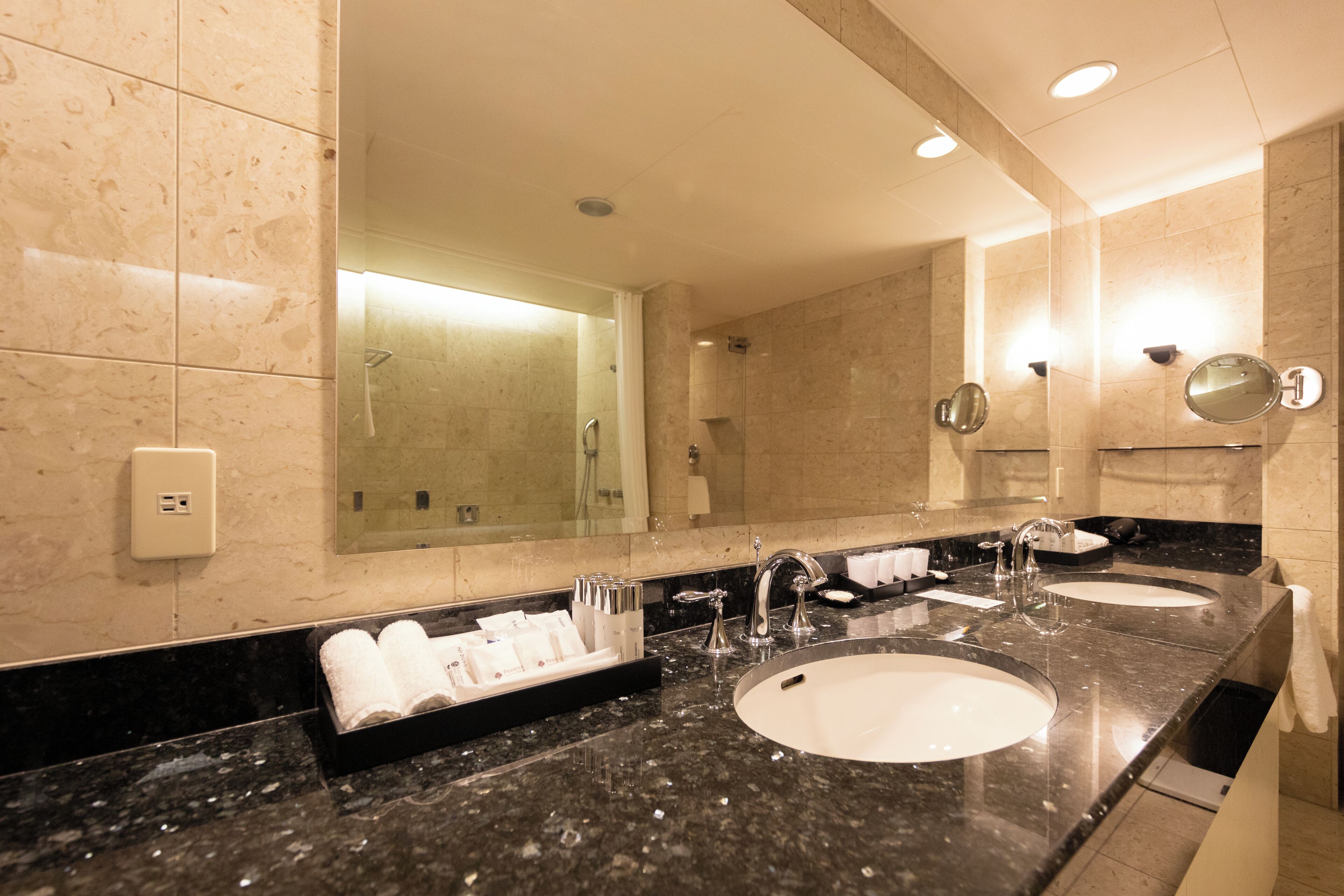 A hotel bathroom with two sinks, a large mirror, and a towel rack with towels.