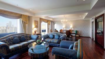 A spacious living room with a large sofa, a smaller sofa, and two armchairs. There is a dining area with a table and chairs, and a kitchen area with cabinets and a countertop.