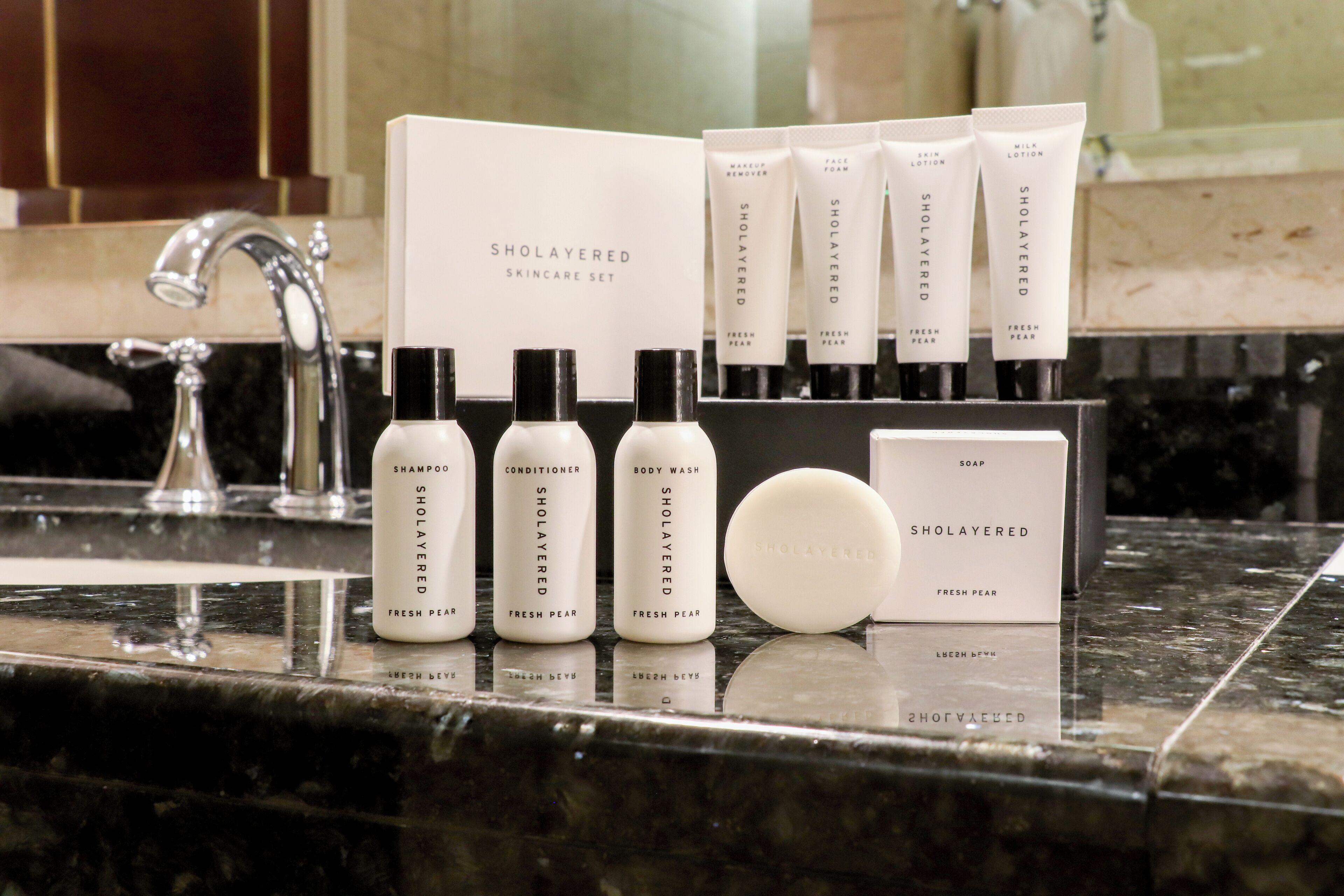 A bathroom counter with a SHOLAYERED SKINCARE SET including shampoo, conditioner, body wash, soap, and lotion.