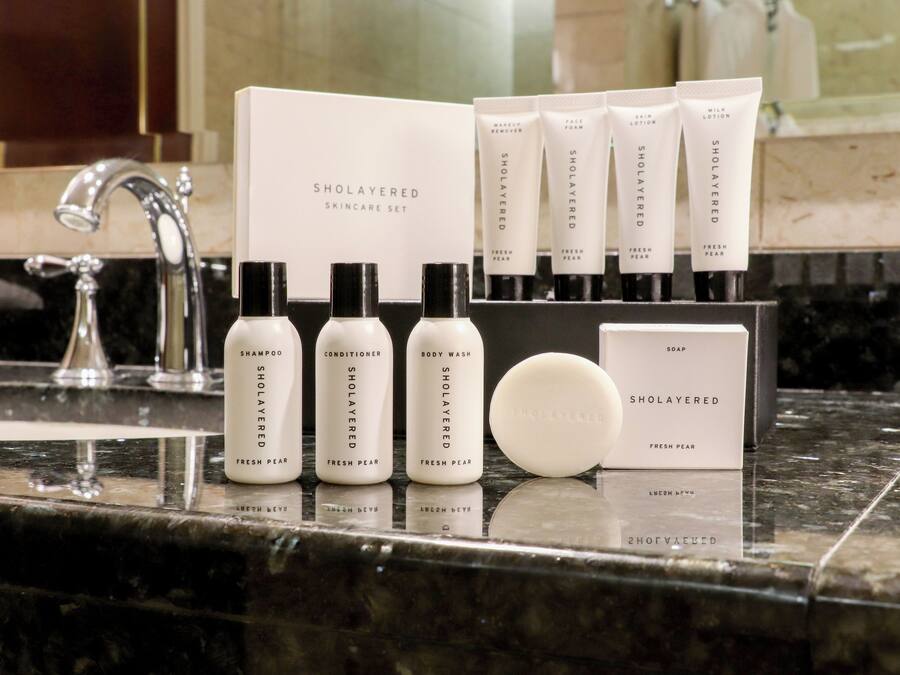 A bathroom counter with a SHOLAYERED SKINCARE SET including shampoo, conditioner, body wash, soap, and lotion.
