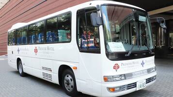 A white bus with "Premier Hotel Tsukaki Sapporo" branding, parked in front of a building.