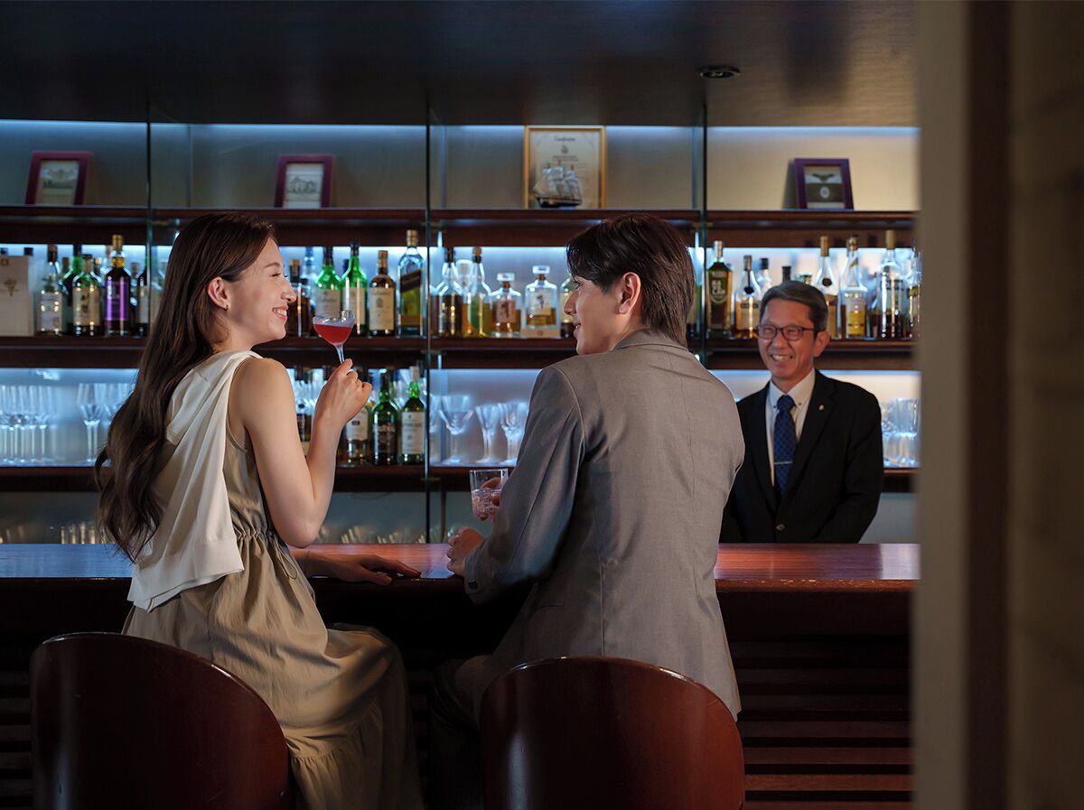 A bar area with a counter, shelves of bottles, and glasses.