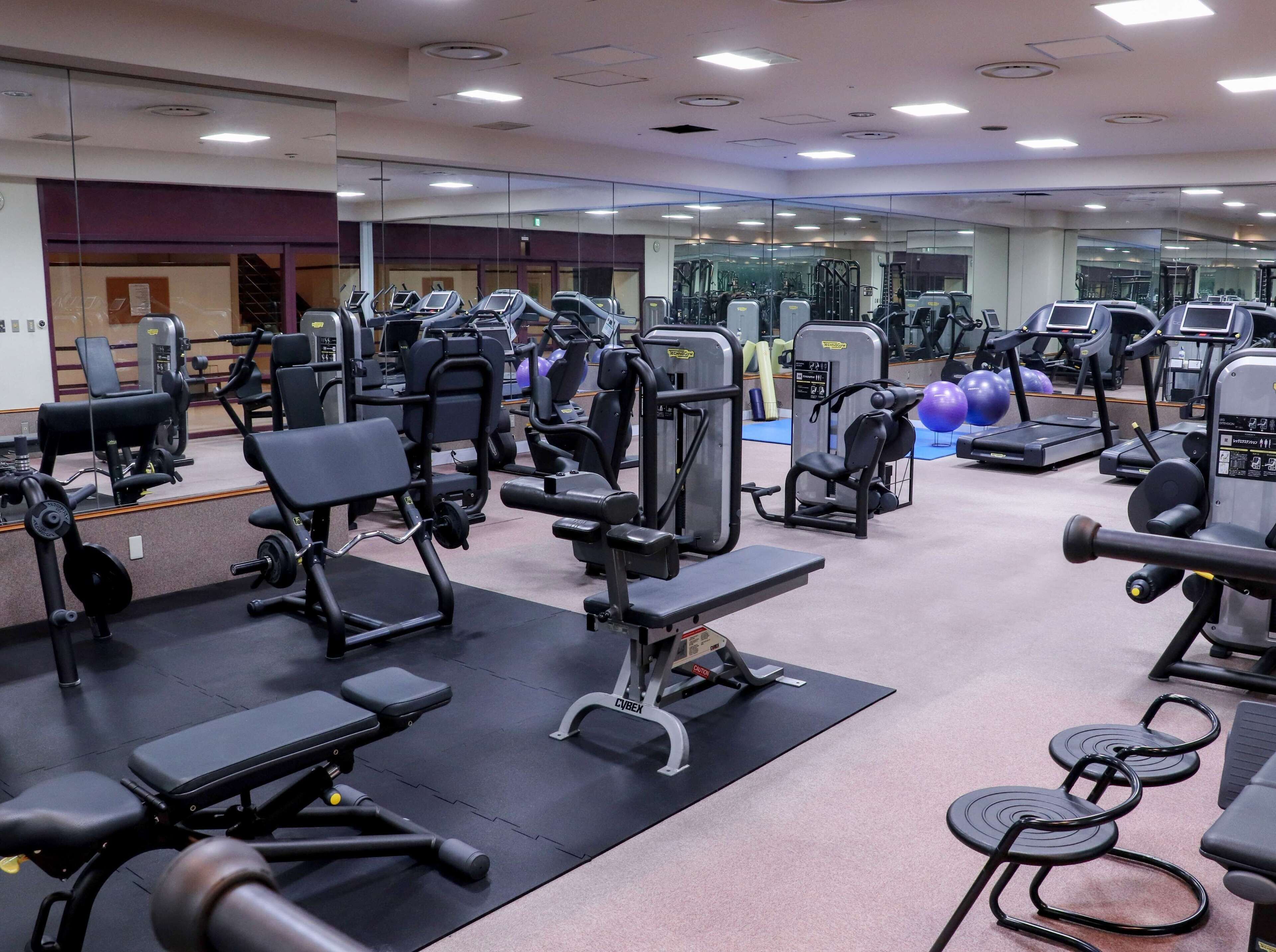 Un gimnasio con diversas máquinas de ejercicio, espejos y pelotas de entrenamiento.