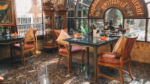 A restaurant interior with a marble floor, wooden furniture, and a large arched window. - Ammata Lanta Resort (Bang Phli)