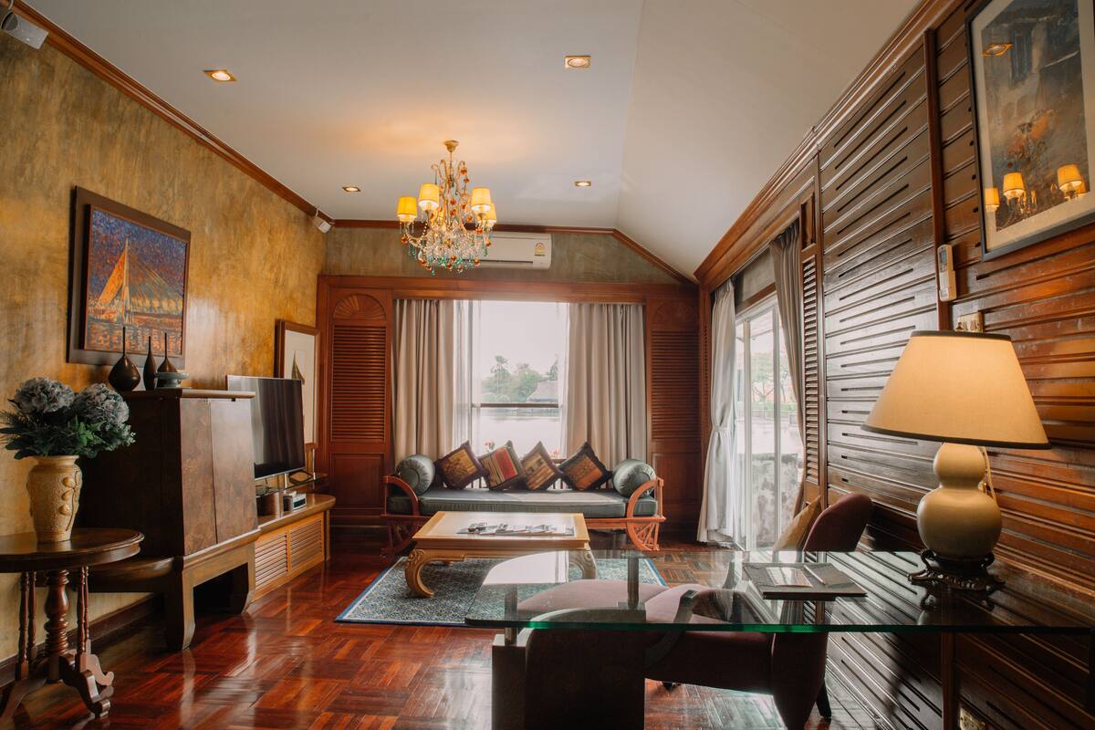 A spacious living room with a wooden floor, a glass coffee table, a sofa with cushions, a television, and a chandelier.