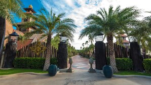 A pathway lined with palm trees and a wooden fence leading to a building with a red roof. - Ammata Lanta Resort (Bang Phli)