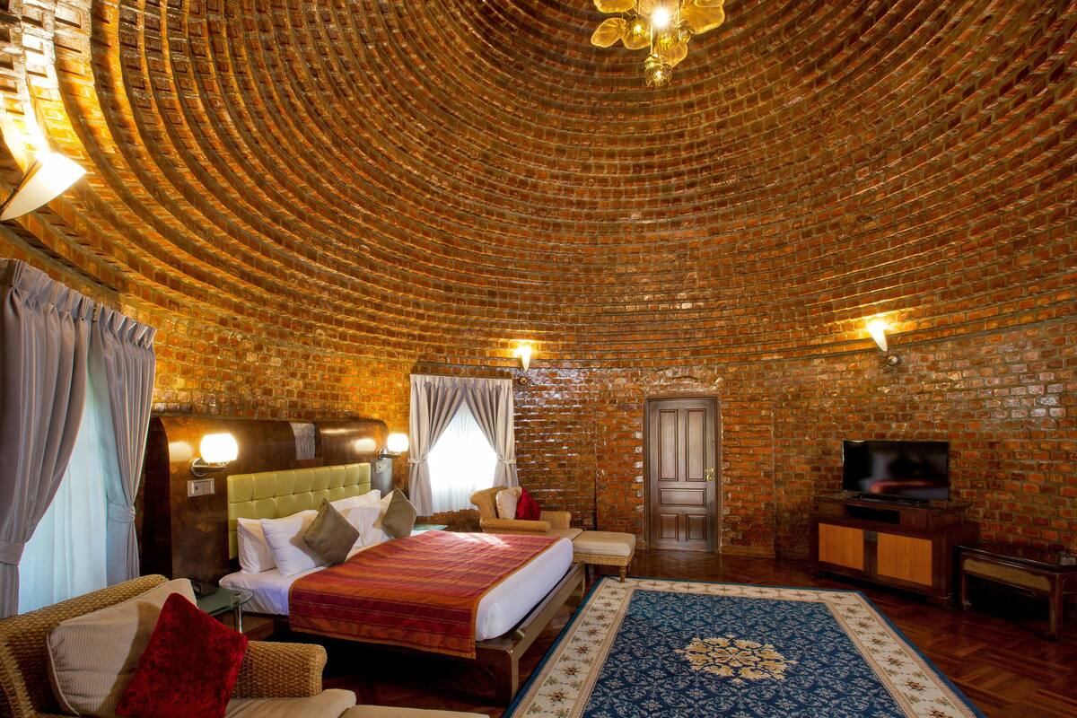 A room with a brick ceiling, a bed with a red blanket, a television, and a wooden cabinet.