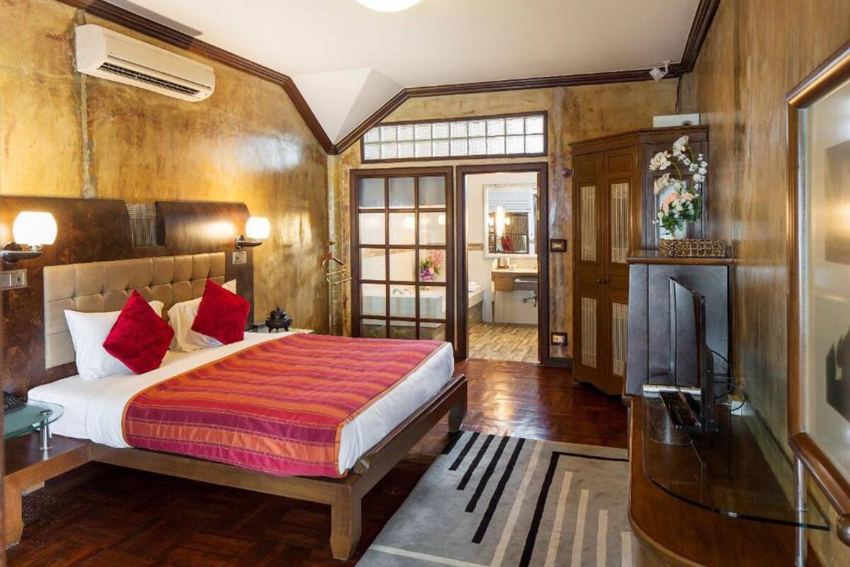 A hotel room with a large bed, wooden flooring, a TV, and a bathroom visible through an open door.