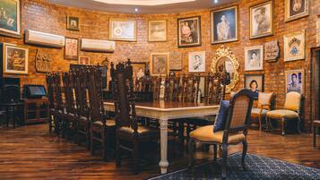 A dining area with a long wooden table surrounded by ornate chairs, a patterned rug, and a brick wall adorned with framed pictures.