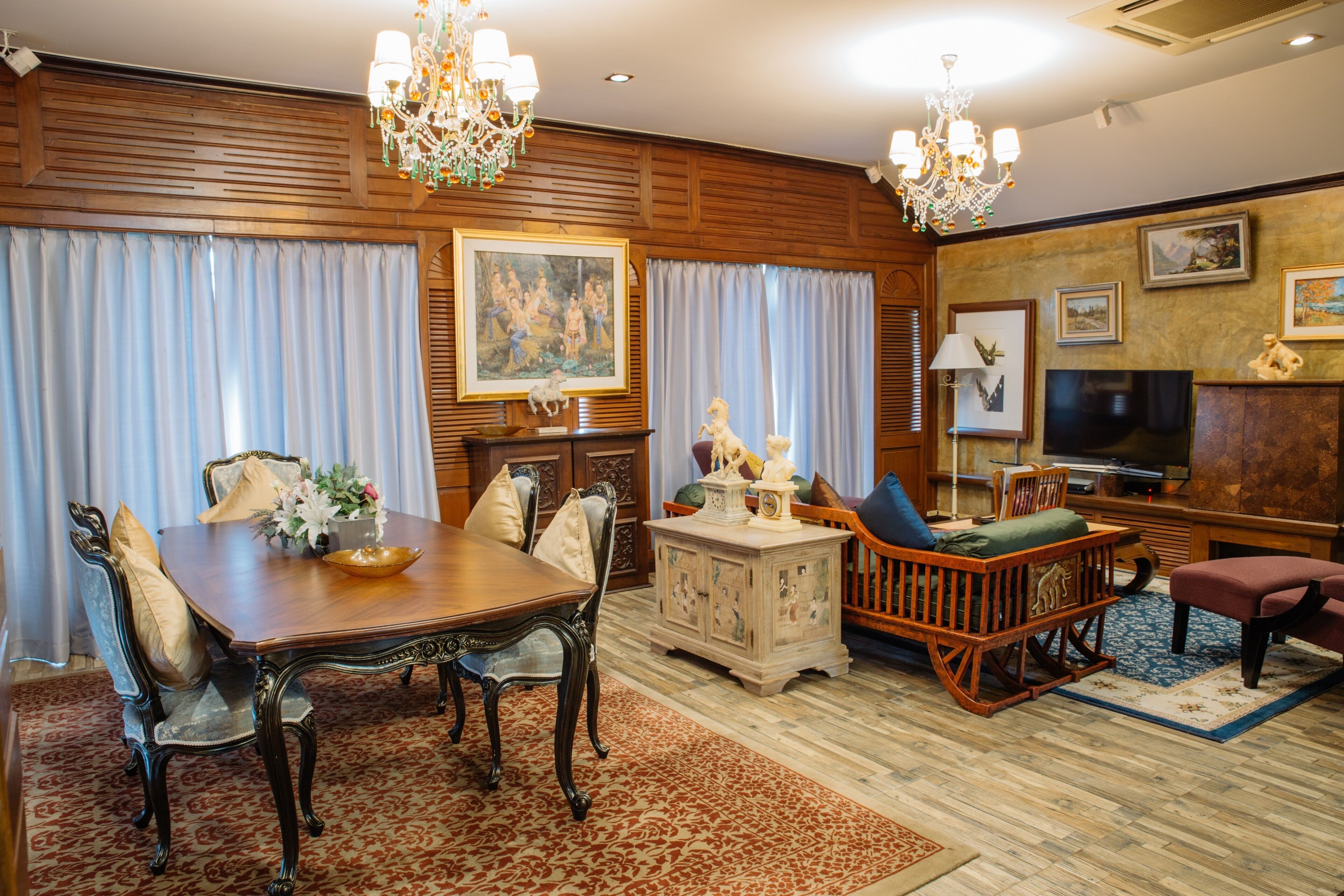 A traditional dining room with a wooden table, chairs, and a chandelier. There is a television and a fireplace in the living area.