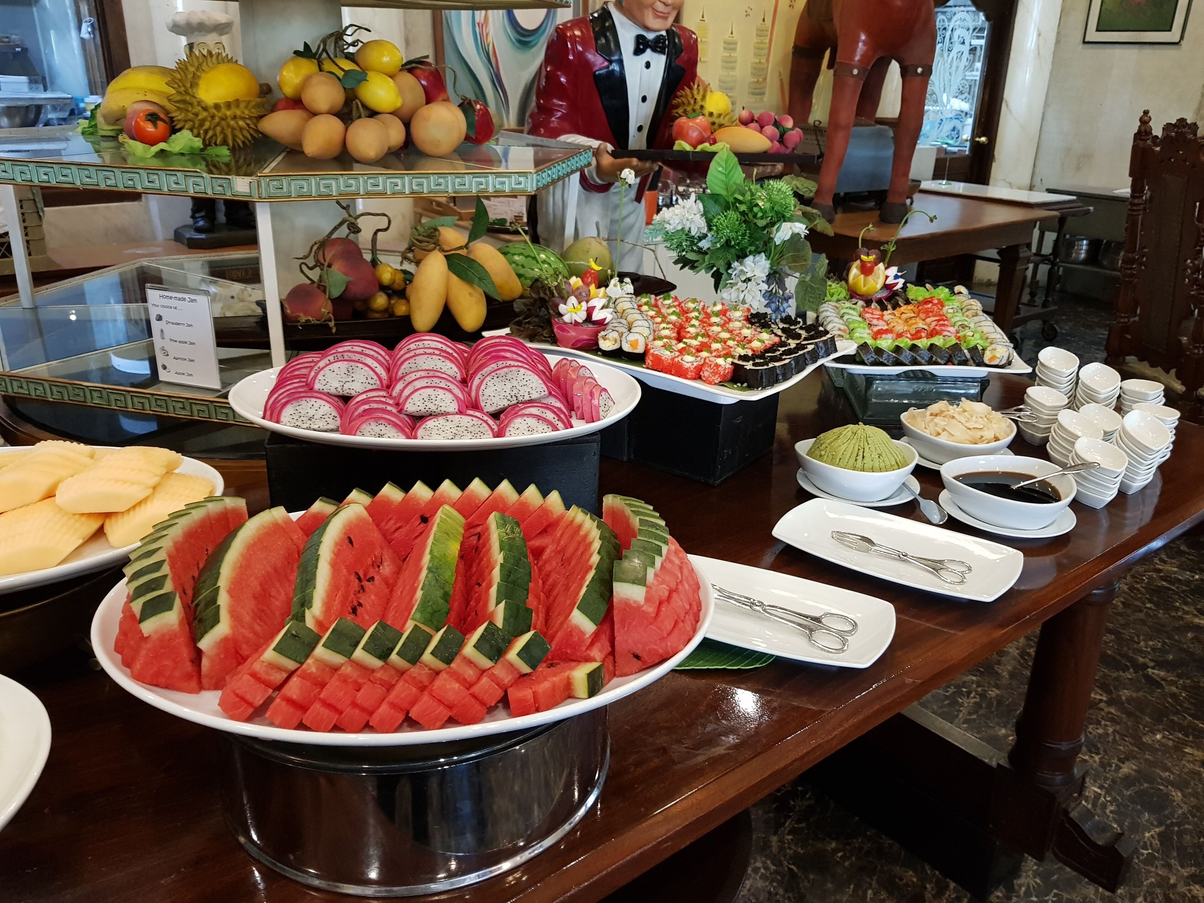A buffet with various food items including watermelon slices, dragon fruit, and sushi.