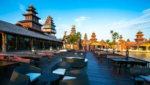 A wooden deck with wicker furniture and a view of traditional pagoda-style buildings. - Ammata Lanta Resort (Bang Phli)