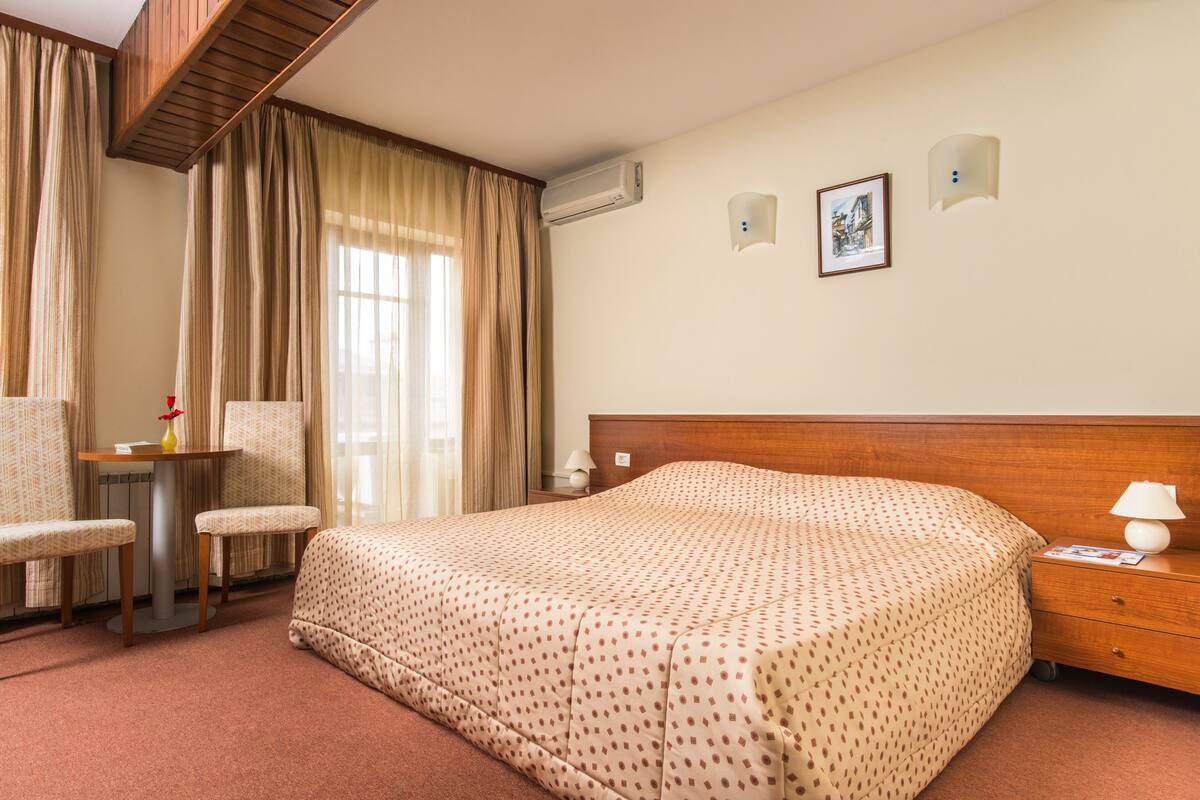 Quarto de hotel com cama, escrivaninha, cadeira, mesa pequena e mesa de cabeceira.