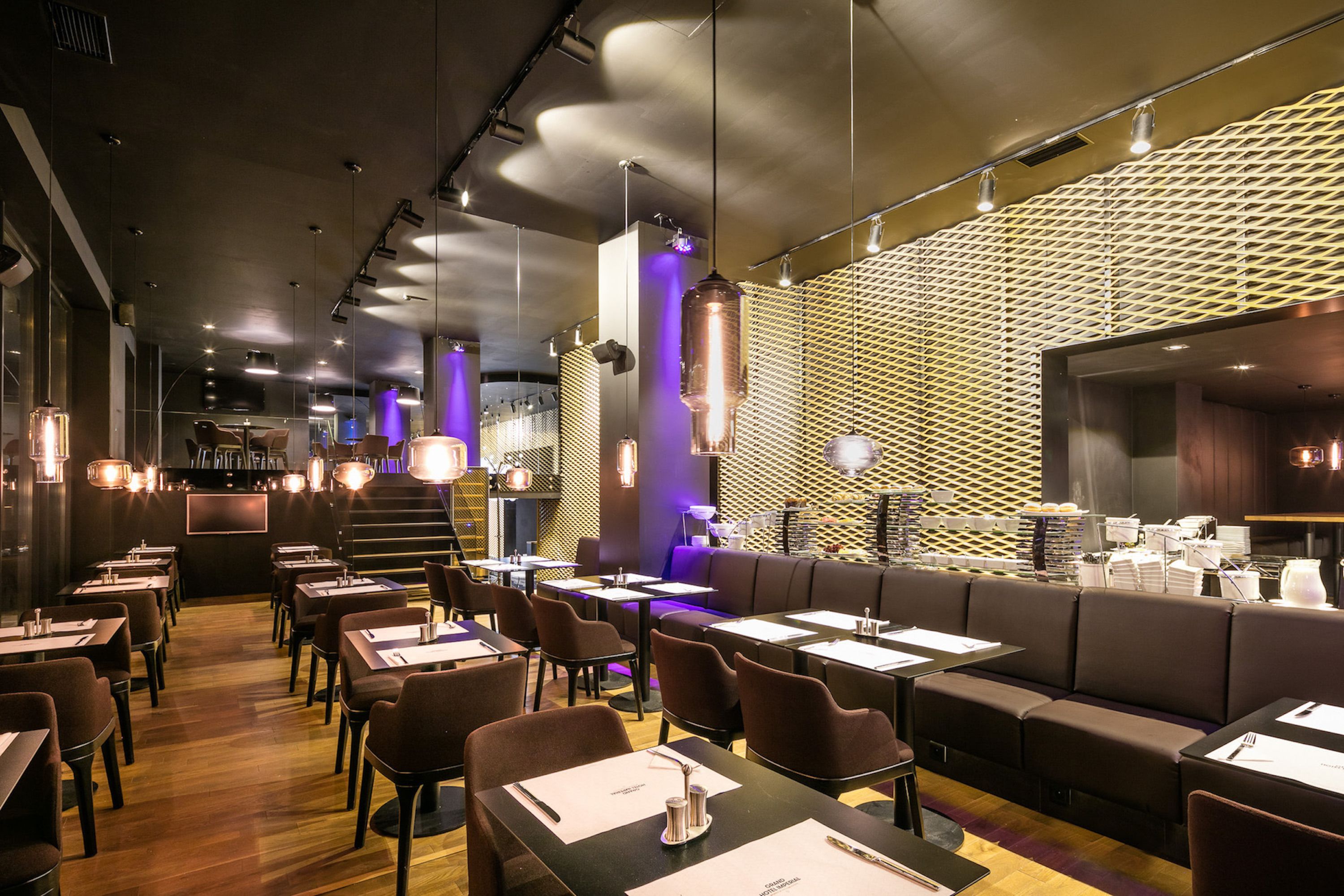 A modern restaurant with a mix of booths and tables, a patterned wall, and pendant lighting.