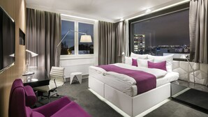 A modern hotel room with a large bed, a desk, and a chair. There is a window with a view of the city at night. - Pytloun Grand Hotel Imperial (Liberec)