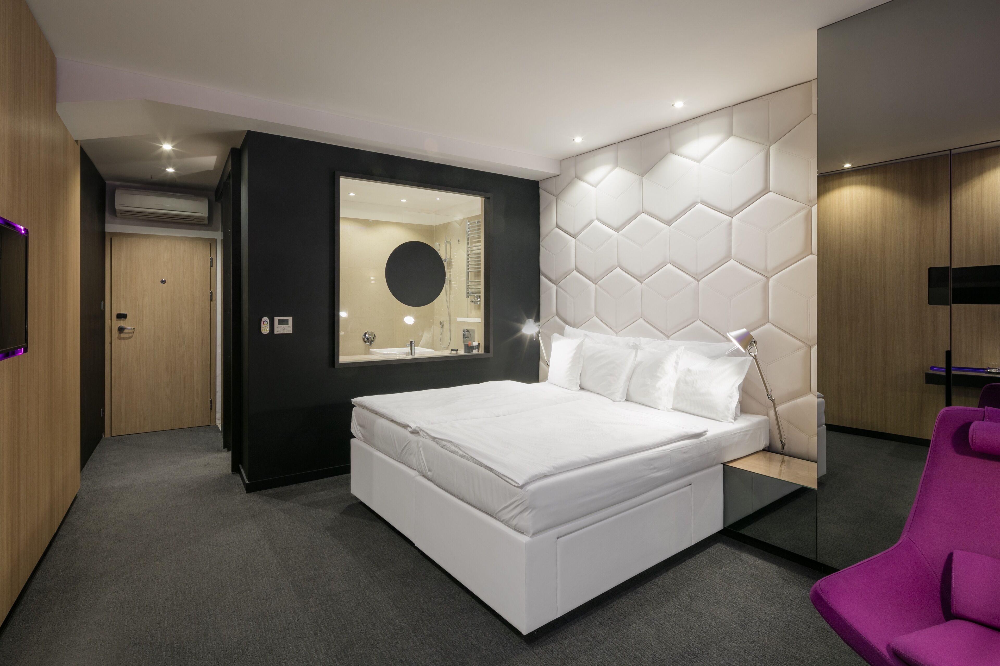 Un dormitorio moderno con una cama grande, un tocador con espejo y un diseño de pared hexagonal original.