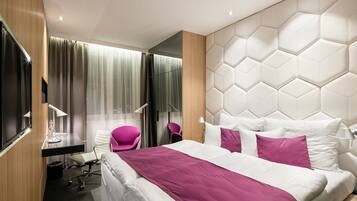 A modern hotel room with a large bed, a desk, a chair, and a television.