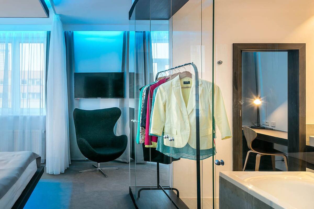 Une chambre d’hôtel moderne équipée d’un lit, d’un coin salon, d’une coiffeuse et d’un portant à vêtements.