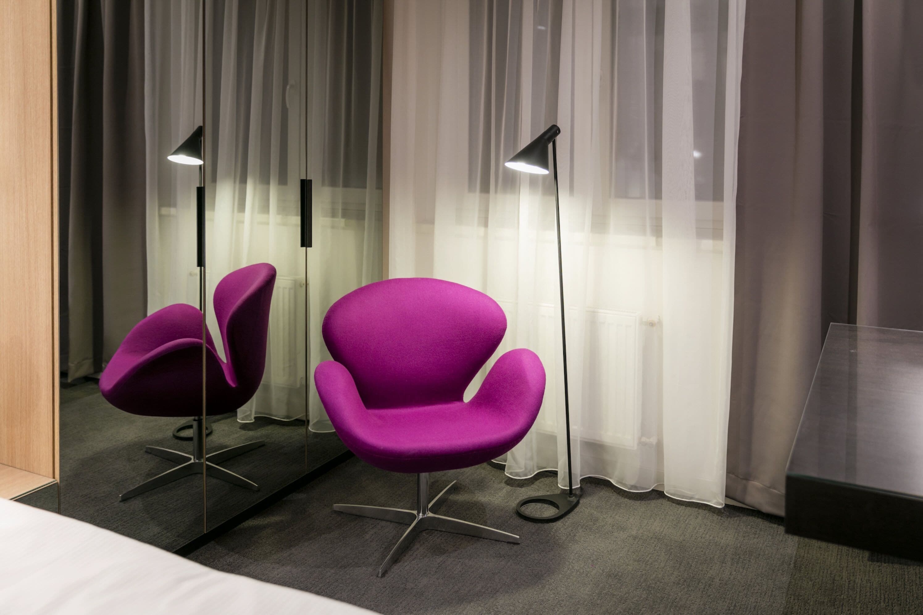 Una habitación de hotel moderna con dos sillas moradas, un espejo grande y una lámpara de pie.