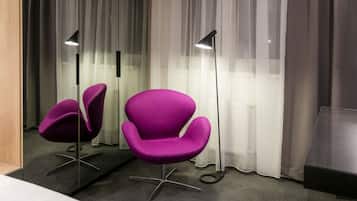 Una habitación de hotel moderna con dos sillas moradas, un espejo grande y una lámpara de pie.