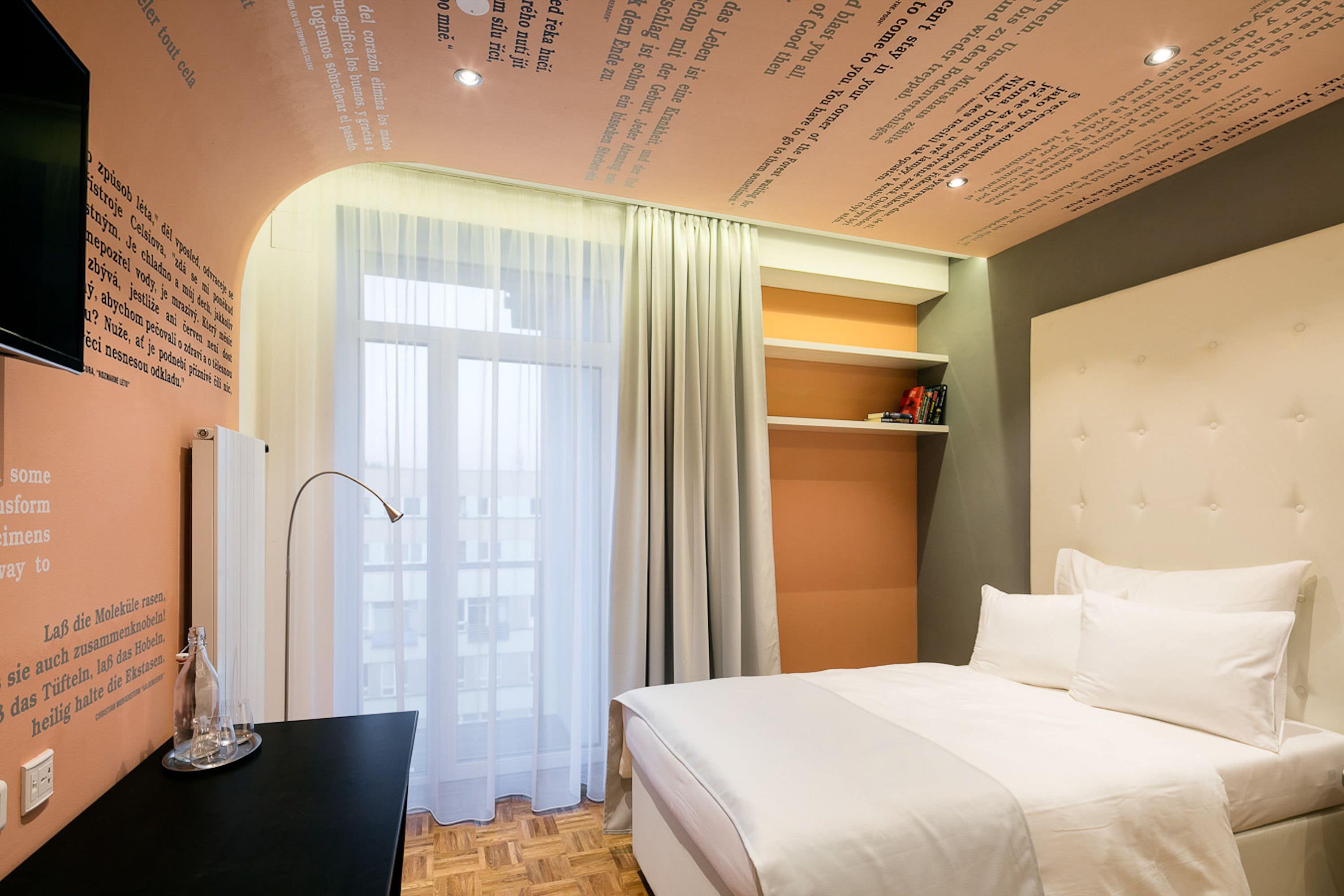 Een hotelkamer met een bed, een bureau, een spiegel en een raam met gordijnen.