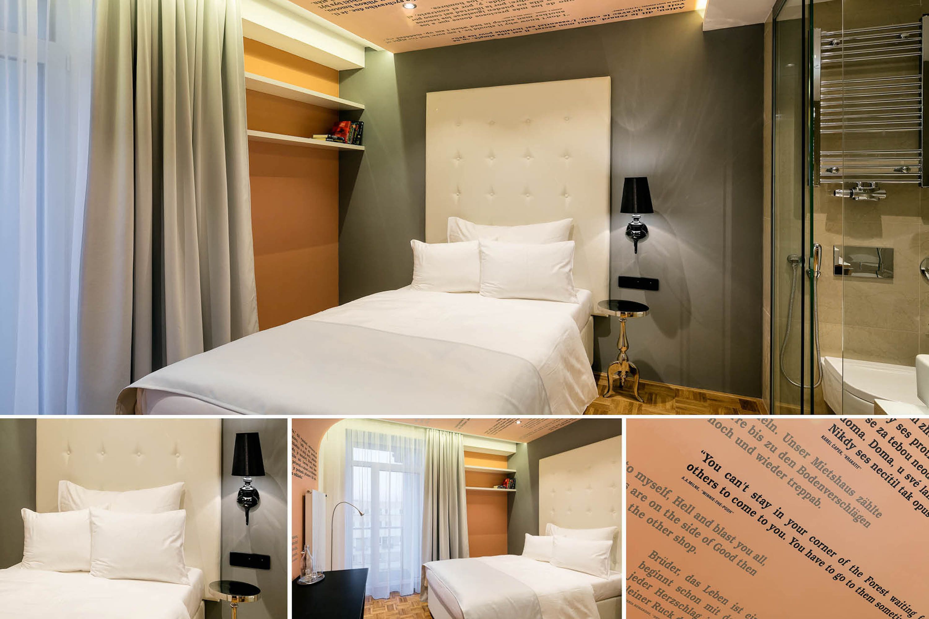 Quarto de hotel com uma cama grande, mesa de cabeceira, luminária, box de vidro para chuveiro e estante com livros.