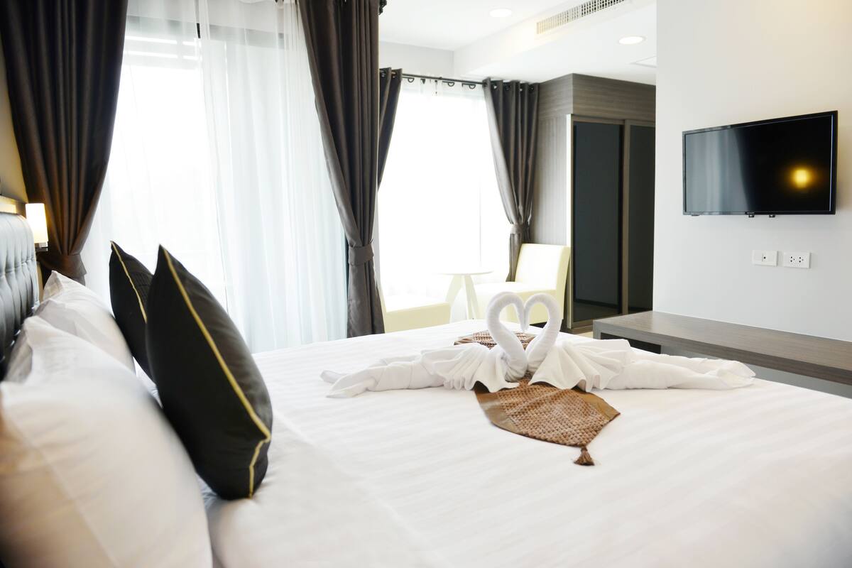 Une chambre d’hôtel avec un lit soigneusement fait, un téléviseur à écran plat fixé au mur et une grande fenêtre avec des rideaux.