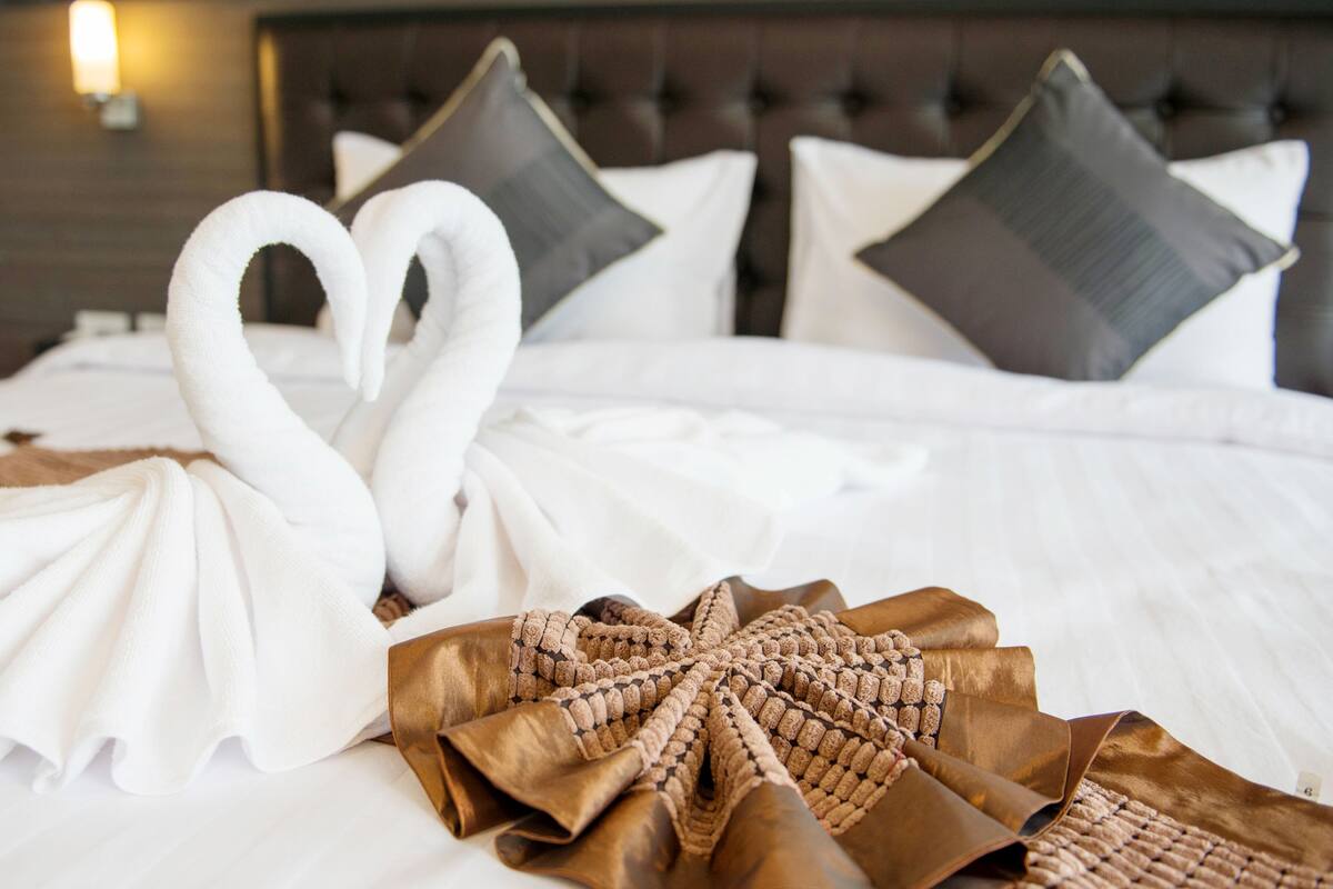 Un lit bien fait, avec du linge de lit blanc et une composition décorative comprenant des serviettes et un ruban brun.