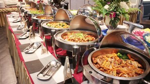 Buffet com diversas estações de comida, cada uma com um recipiente de servir coberto.