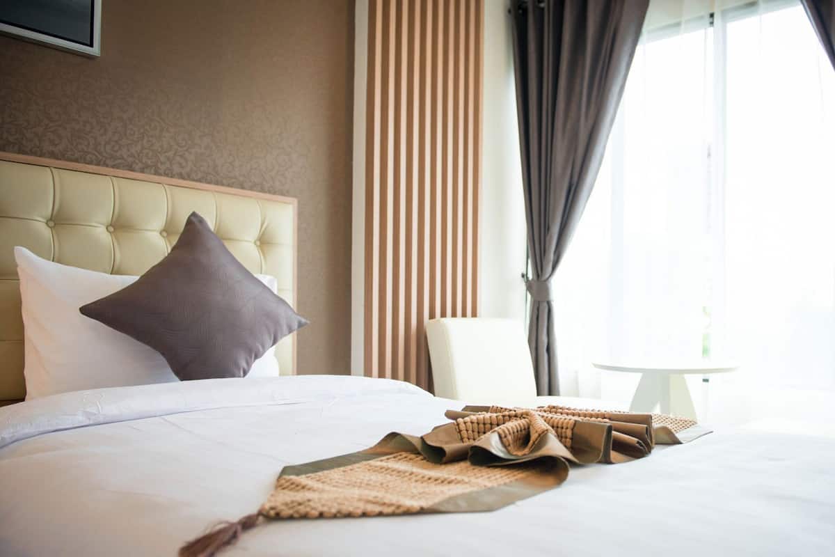 Une chambre d’hôtel avec un grand lit, une tête de lit, une table de chevet, une lampe et une vue sur l’extérieur.