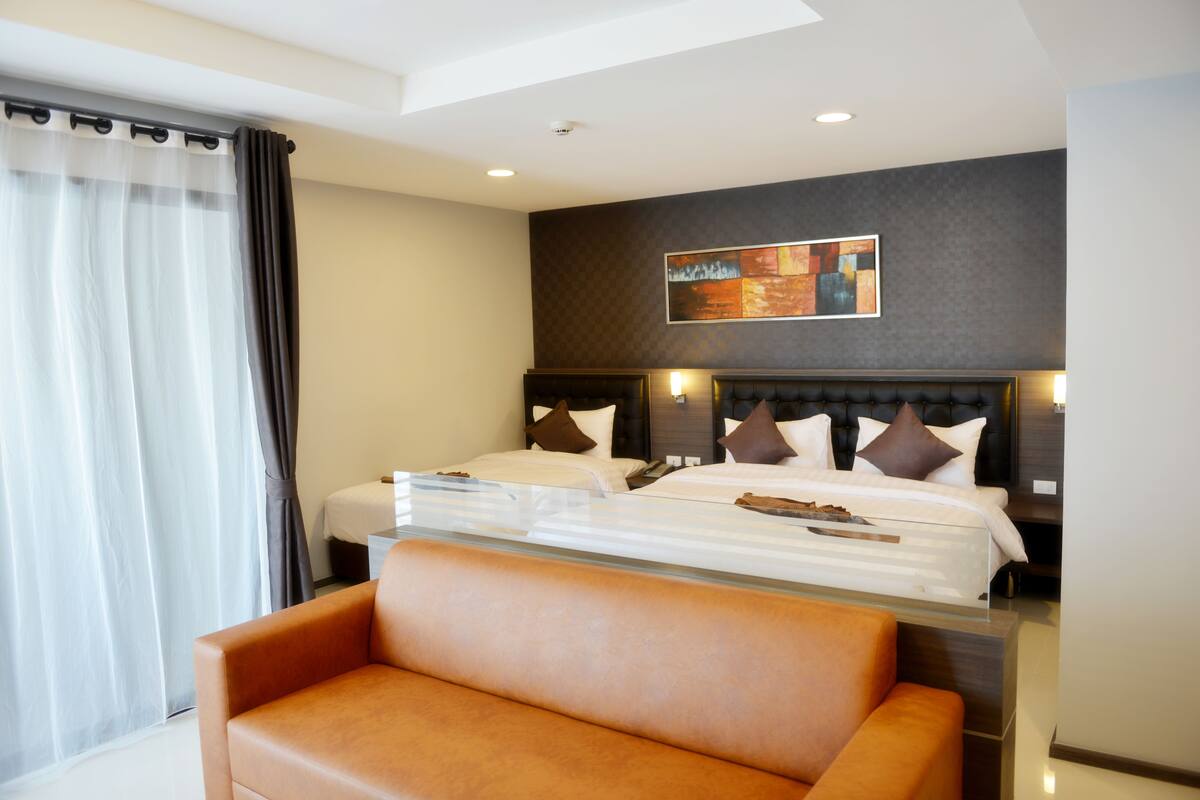 Une chambre d’hôtel avec un grand lit, un canapé, un tableau au mur et une fenêtre avec des rideaux.