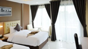 Quarto de hotel com duas camas, um sofá, uma mesa de jantar e uma janela grande com cortinas.